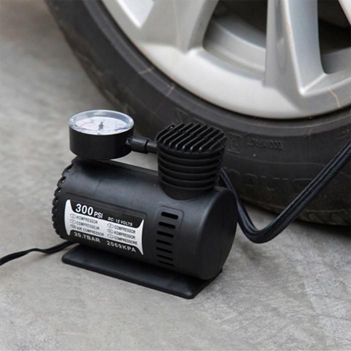 Car tire inflator with pressure gauge next to a car tire on a concrete surface.